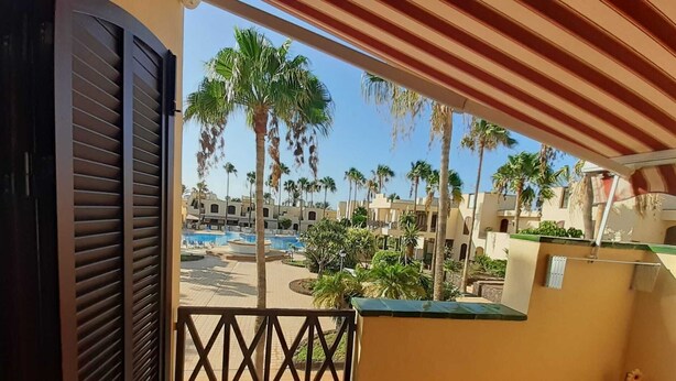 A balcony with a view of a pool area surrounded by palm trees and buildings.