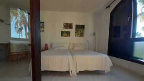 A bedroom with two beds, a desk, and a large window.