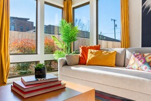 A modern living room with a sofa, cushions, a coffee table, and a plant. - Group-friendly home one mile from Nissan Stadium (Nashville)