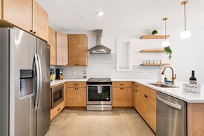 A modern kitchen with stainless steel appliances, wooden cabinets, a built-in oven, and a coffee maker. - Group-friendly home one mile from Nissan Stadium (Nashville)