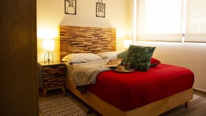 A neatly made bed with a red cover, a wooden headboard, and a bedside table with a lamp.