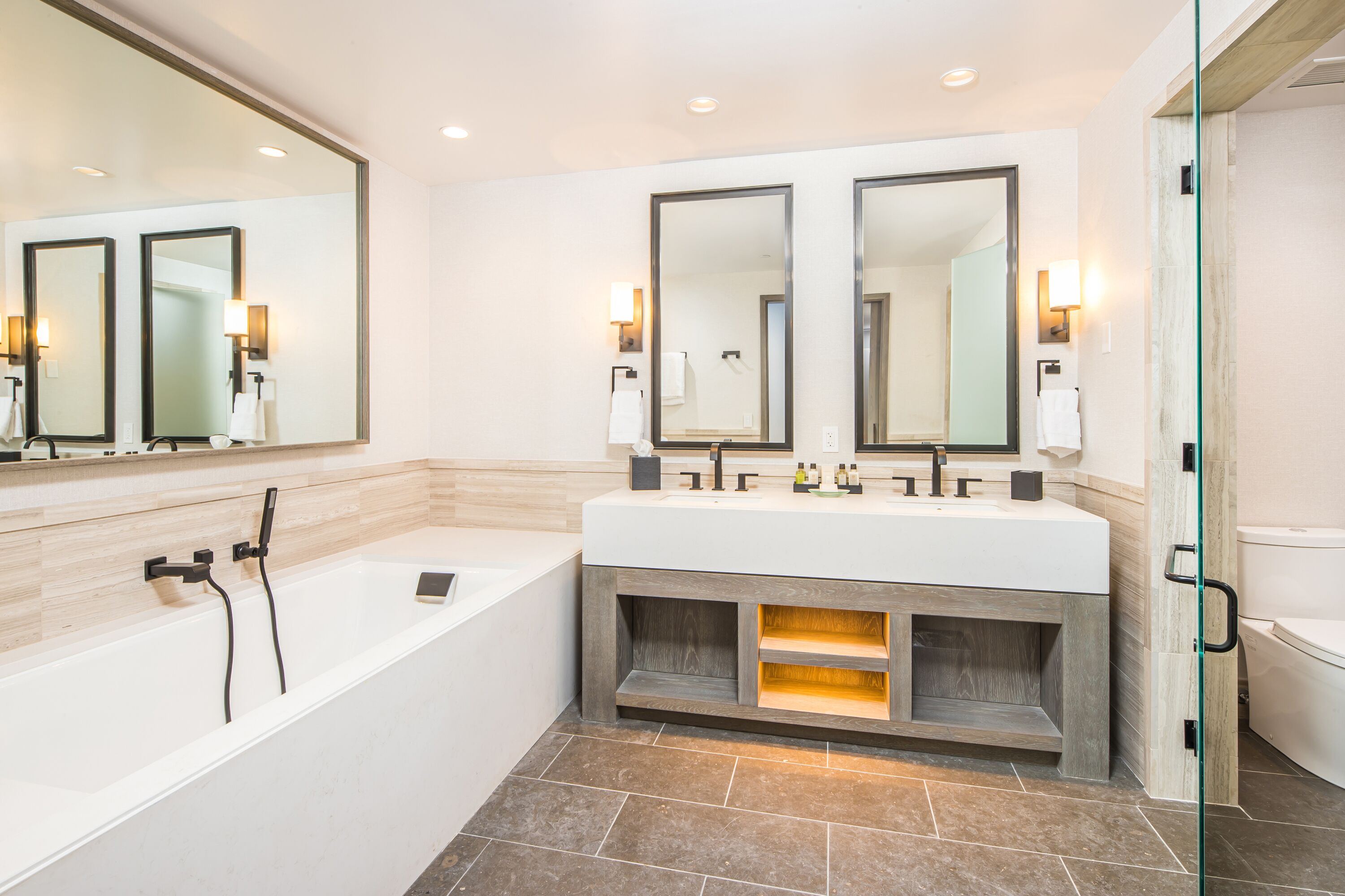 A modern bathroom with a large bathtub, a double sink vanity, and two large mirrors.