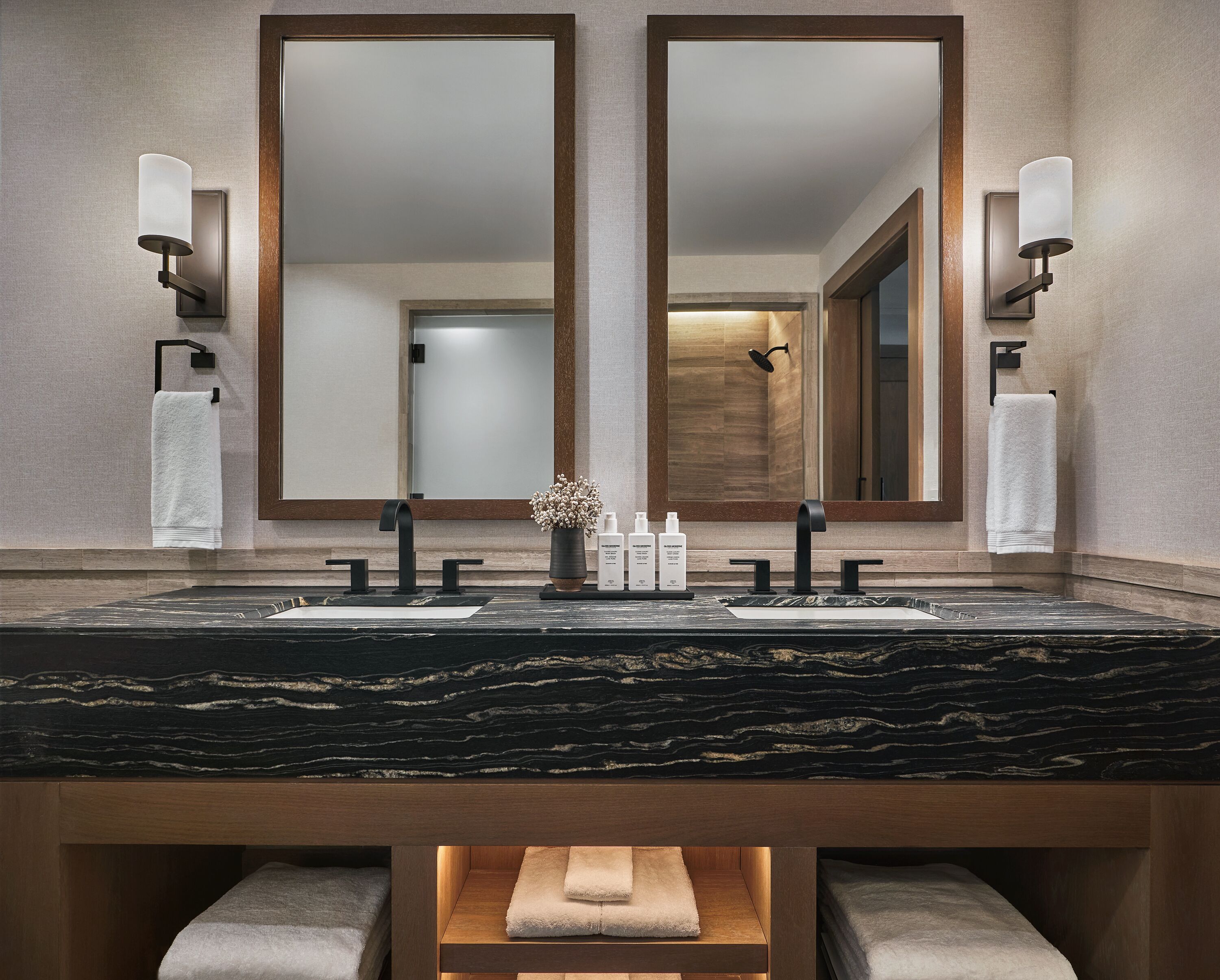 A modern bathroom with a marble sink, two mirrors, and a towel rack.