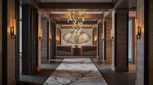 A modern hotel lobby with a marble floor, wooden paneling, and a central chandelier. - Montage Big Sky (Big Sky)