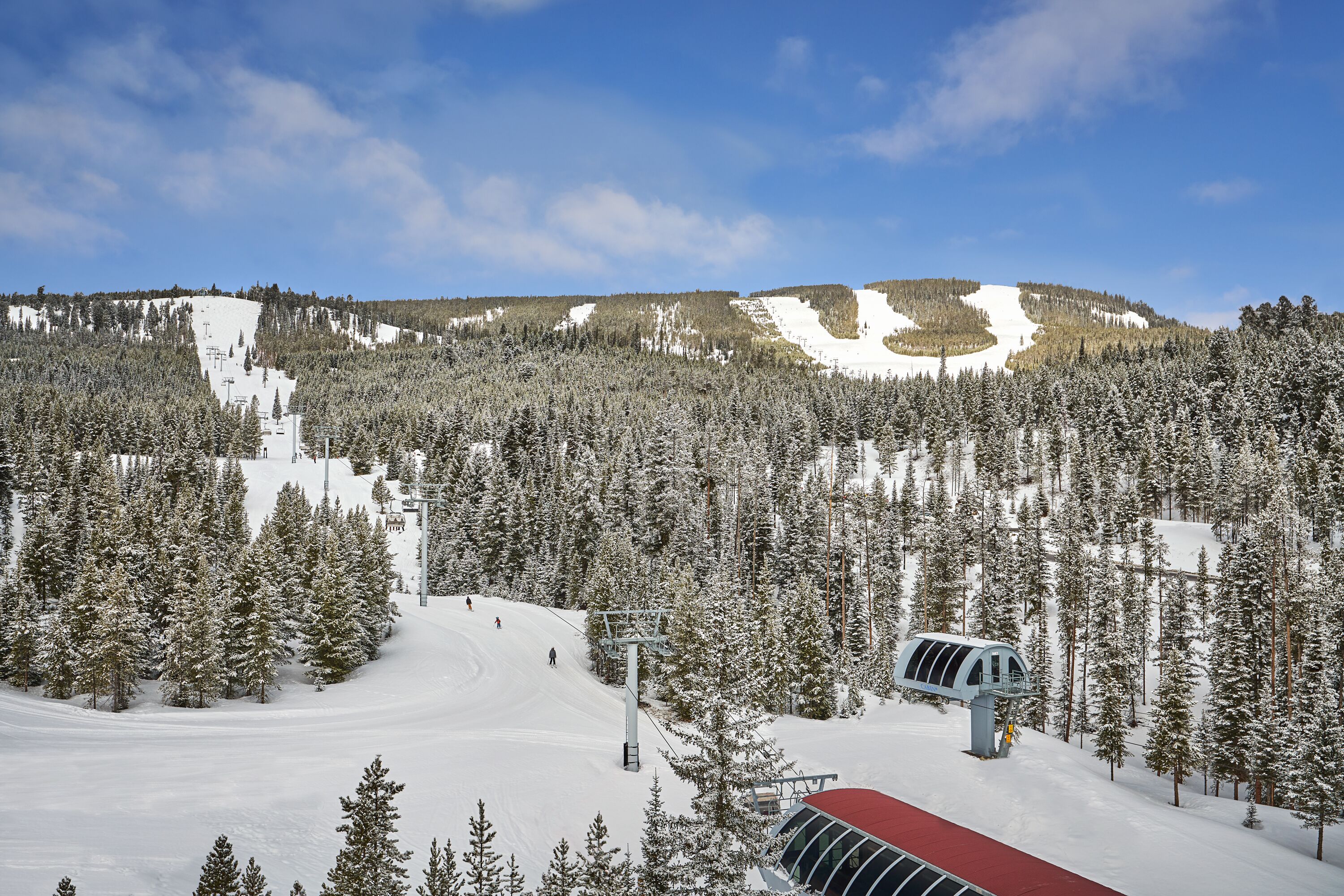 A snow-covered ski slope with a ski lift and a red-roofed building.