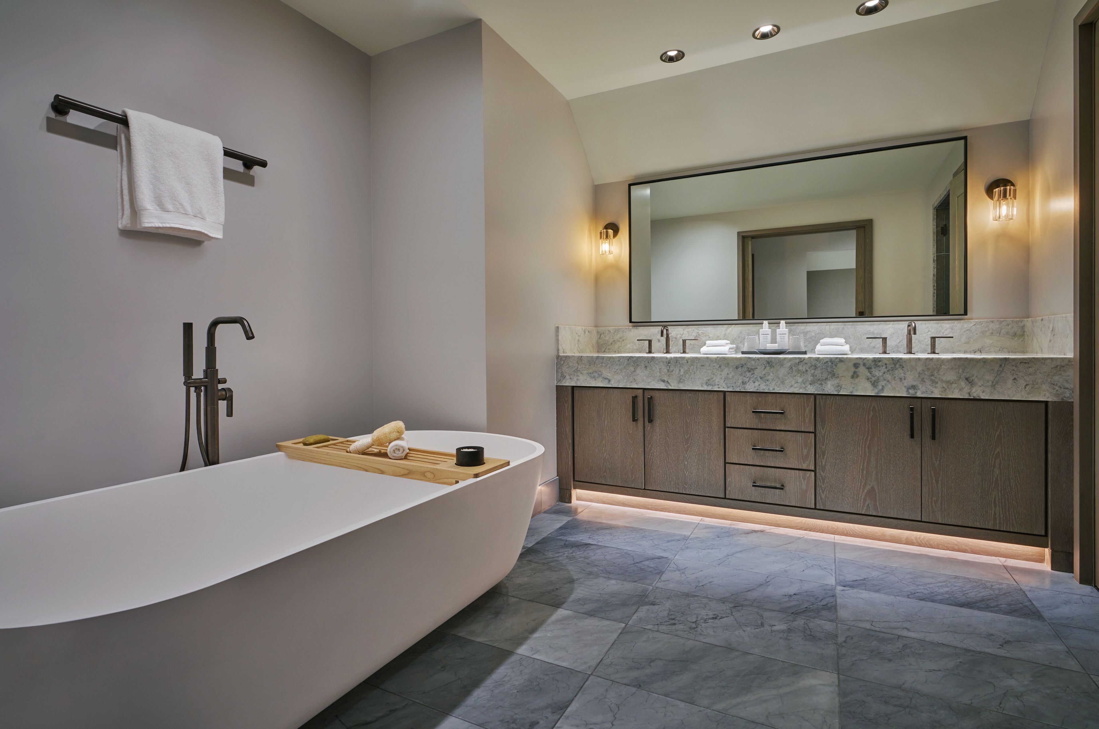 A modern bathroom with a freestanding bathtub, a large mirror, and a vanity with a marble countertop.