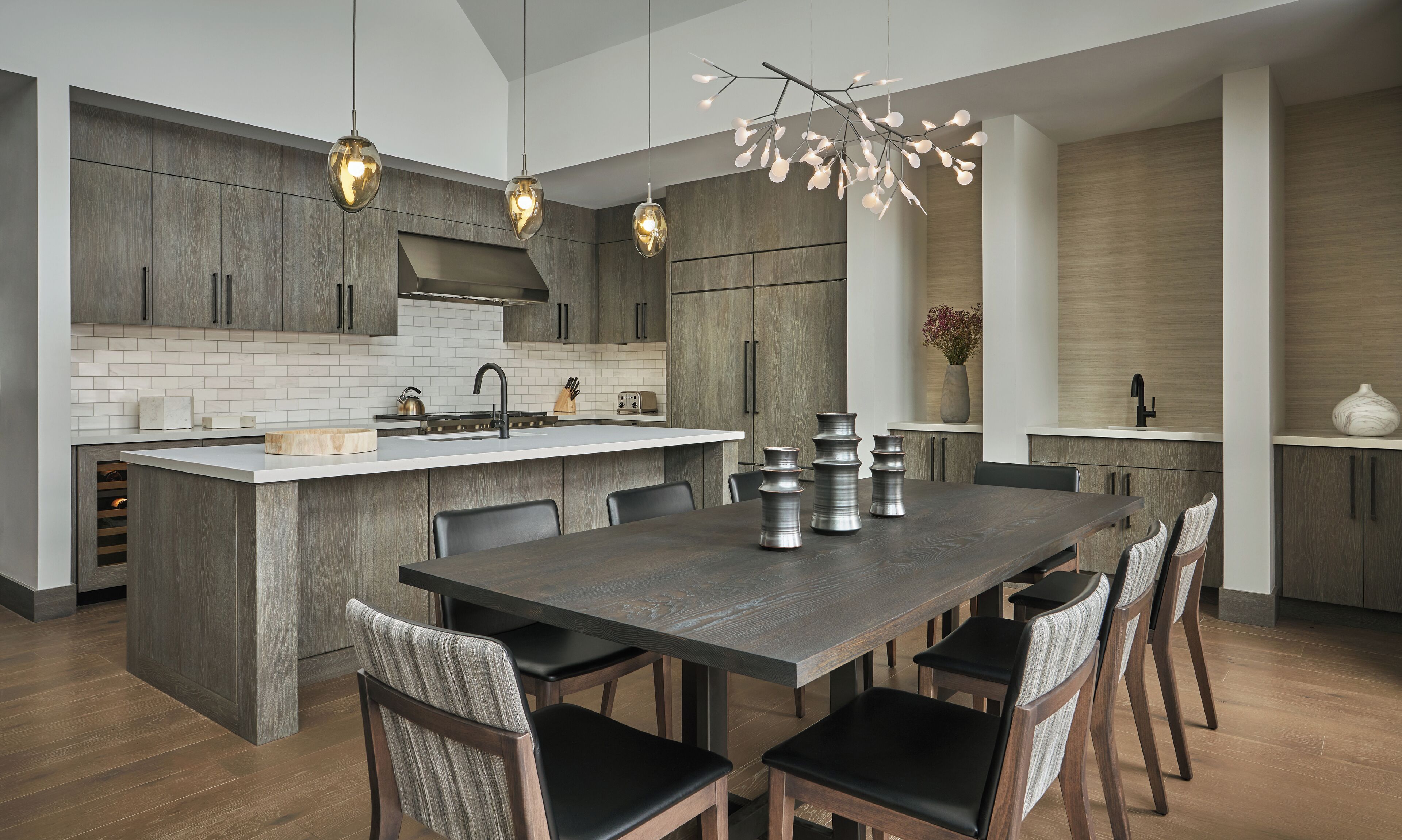 Une cuisine moderne dotée d’un îlot central, de meubles de couleur bois foncé et de luminaires suspendus.