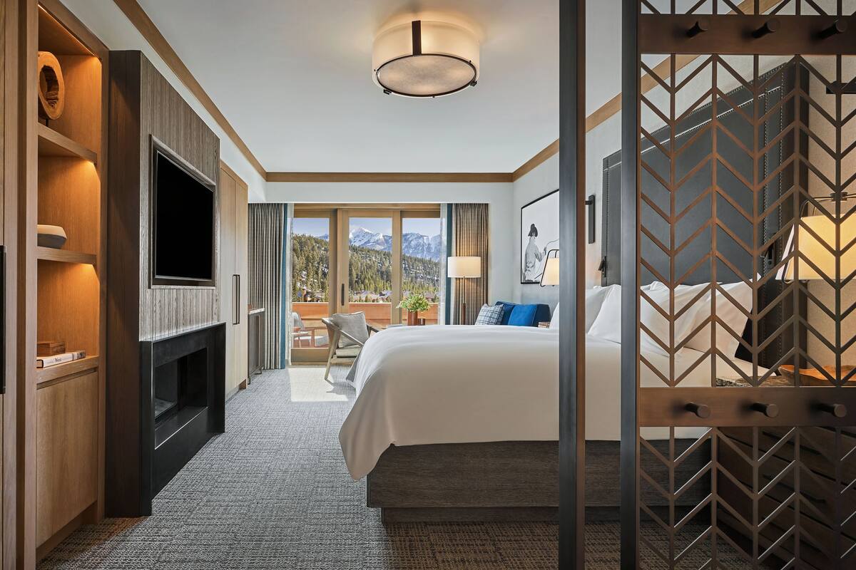 Ein Hotelzimmer mit einem großen Bett, einem Fernseher, einem Kamin und Blick auf die Berge.