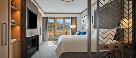 A hotel room with a large bed, a TV, a fireplace, and a view of mountains.