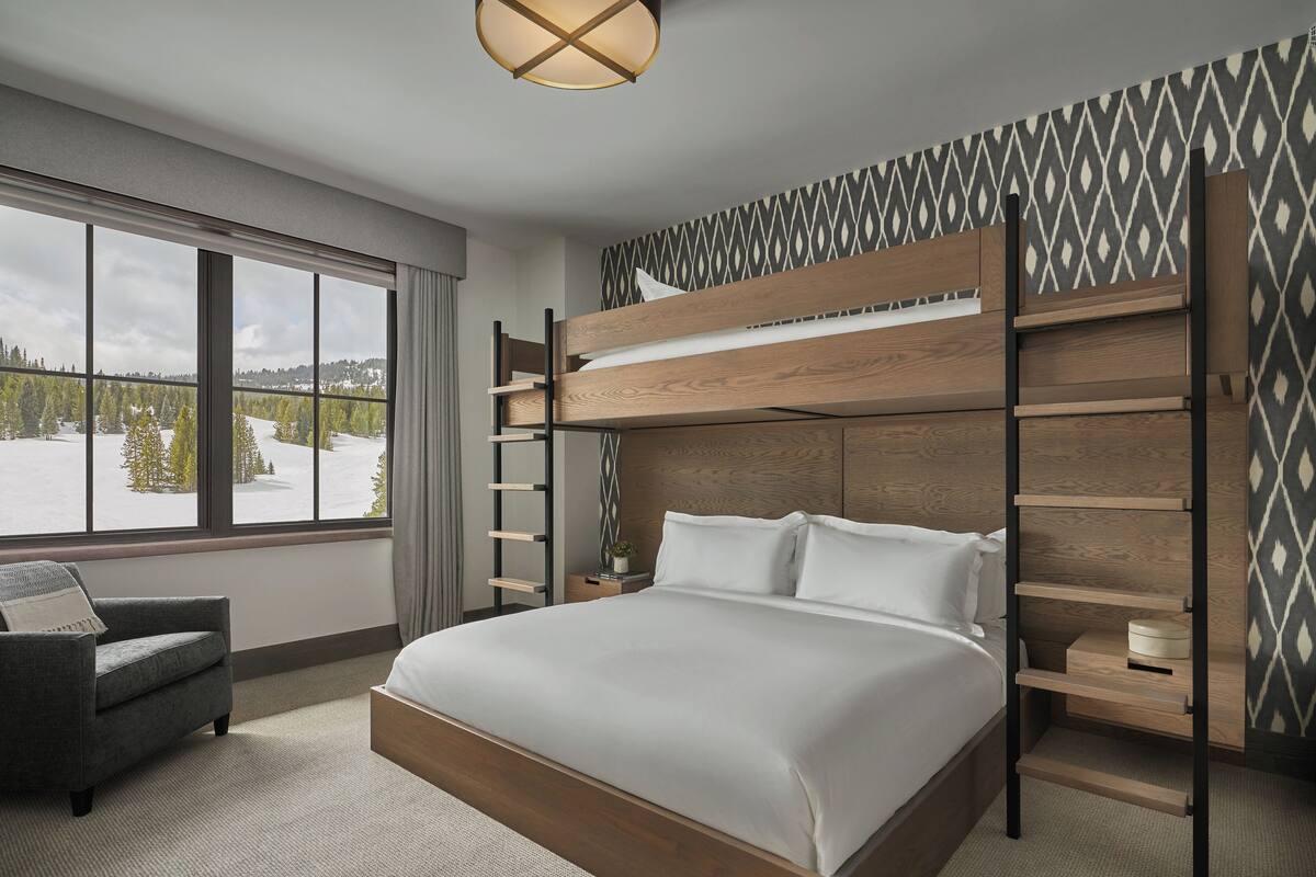 Ein modernes Hotelzimmer mit Etagenbett, großem Fenster und Blick auf eine verschneite Landschaft, einem grauen Sessel und einer Wand mit Muster.