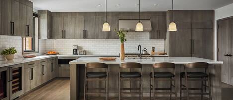 A modern kitchen with dark wood cabinets, a central island with bar stools, pendant lighting, and a white backsplash.