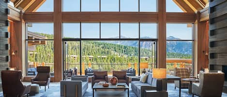 A spacious lobby with large windows offering mountain views, wooden beams, and modern furniture.