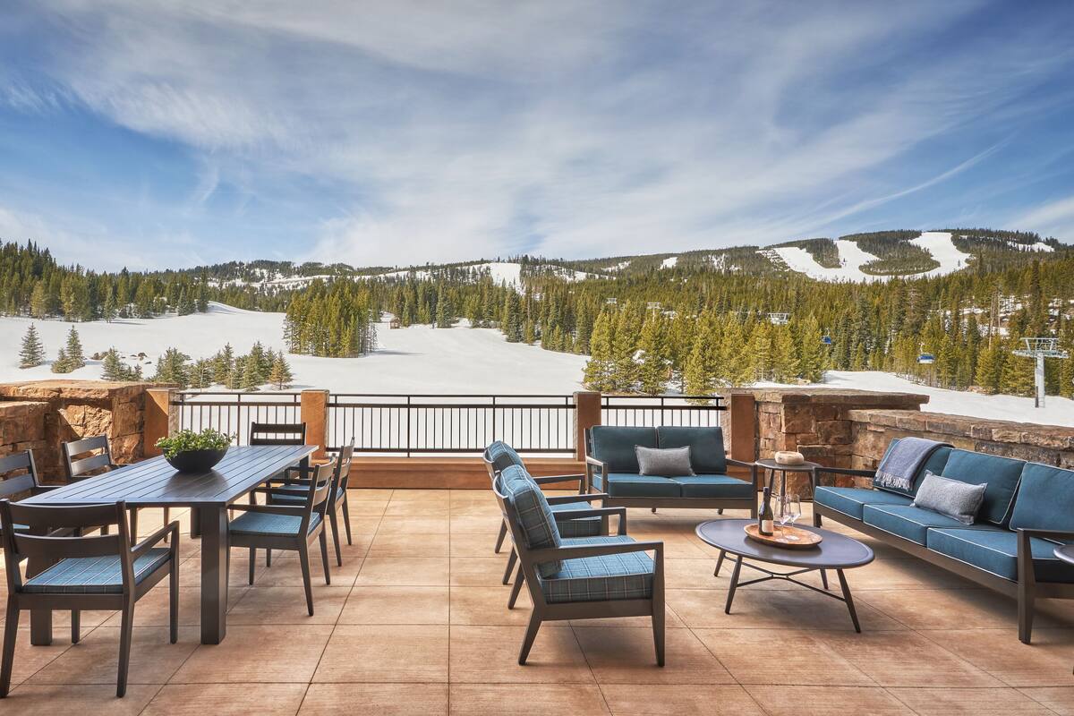 Eine Terrasse mit Tisch, Stühlen und einer Sitzecke mit Blick auf eine verschneite Berglandschaft.