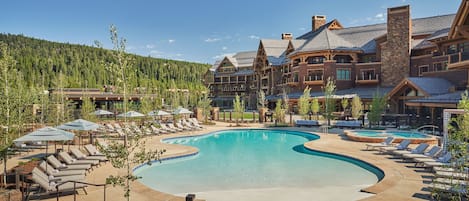 A resort with a large pool, lounge chairs, and a mountainous backdrop.