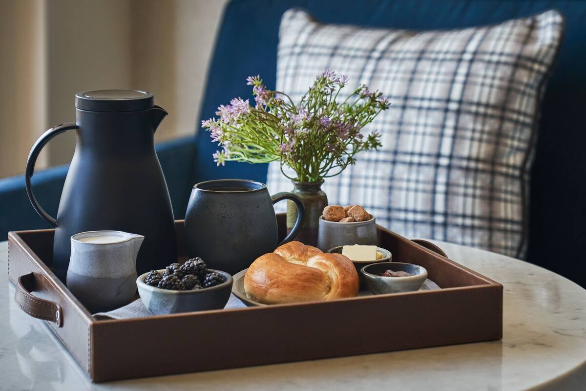 Ein Tablett mit Kaffeekanne, Tassen, einer Blumenvase, einem Croissant und kleinen Schalen mit Speisen.