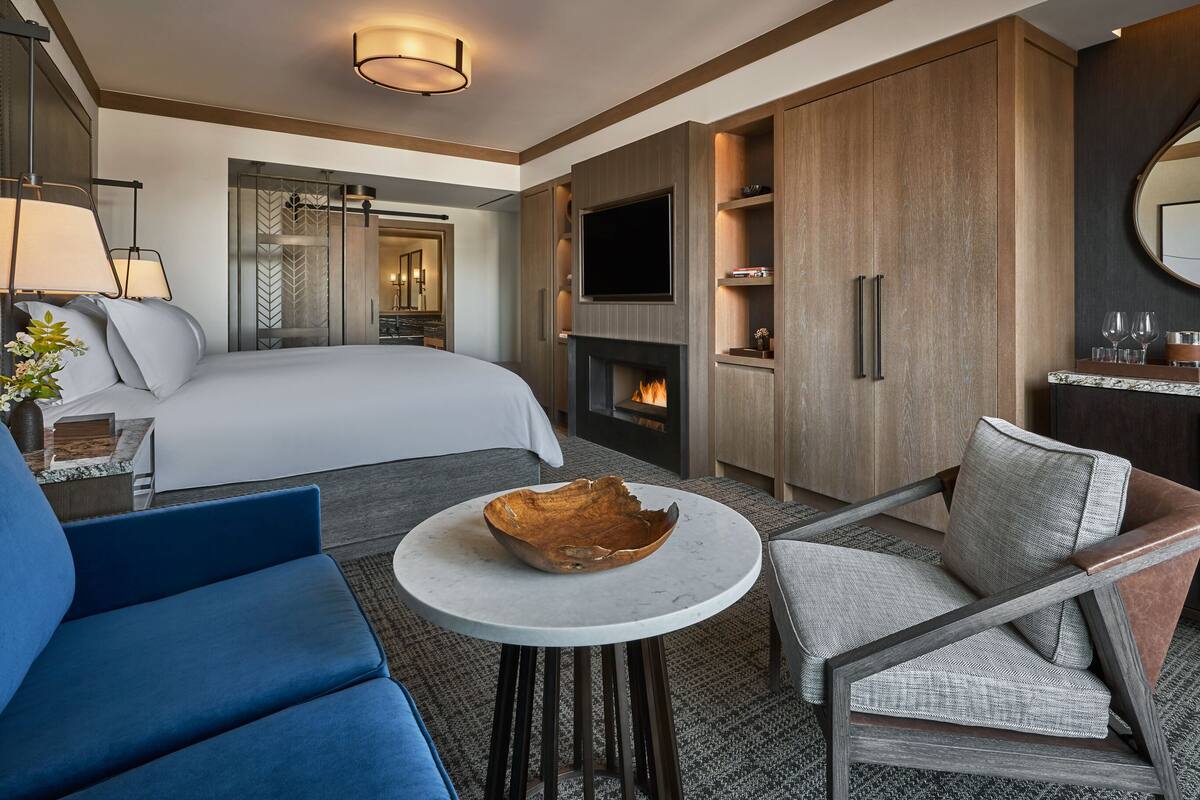 Ein modernes Hotelzimmer mit einem großen Bett, einem Fernseher, einem Kamin, einem Essbereich mit Tisch und Stühlen sowie einem Spiegel an der Wand.