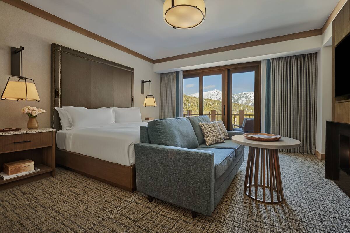 Ein Hotelzimmer mit einem großen Bett, einer Sitzecke, einem kleinen Tisch, einem Fernseher, einem Kamin und Blick auf die Berge.