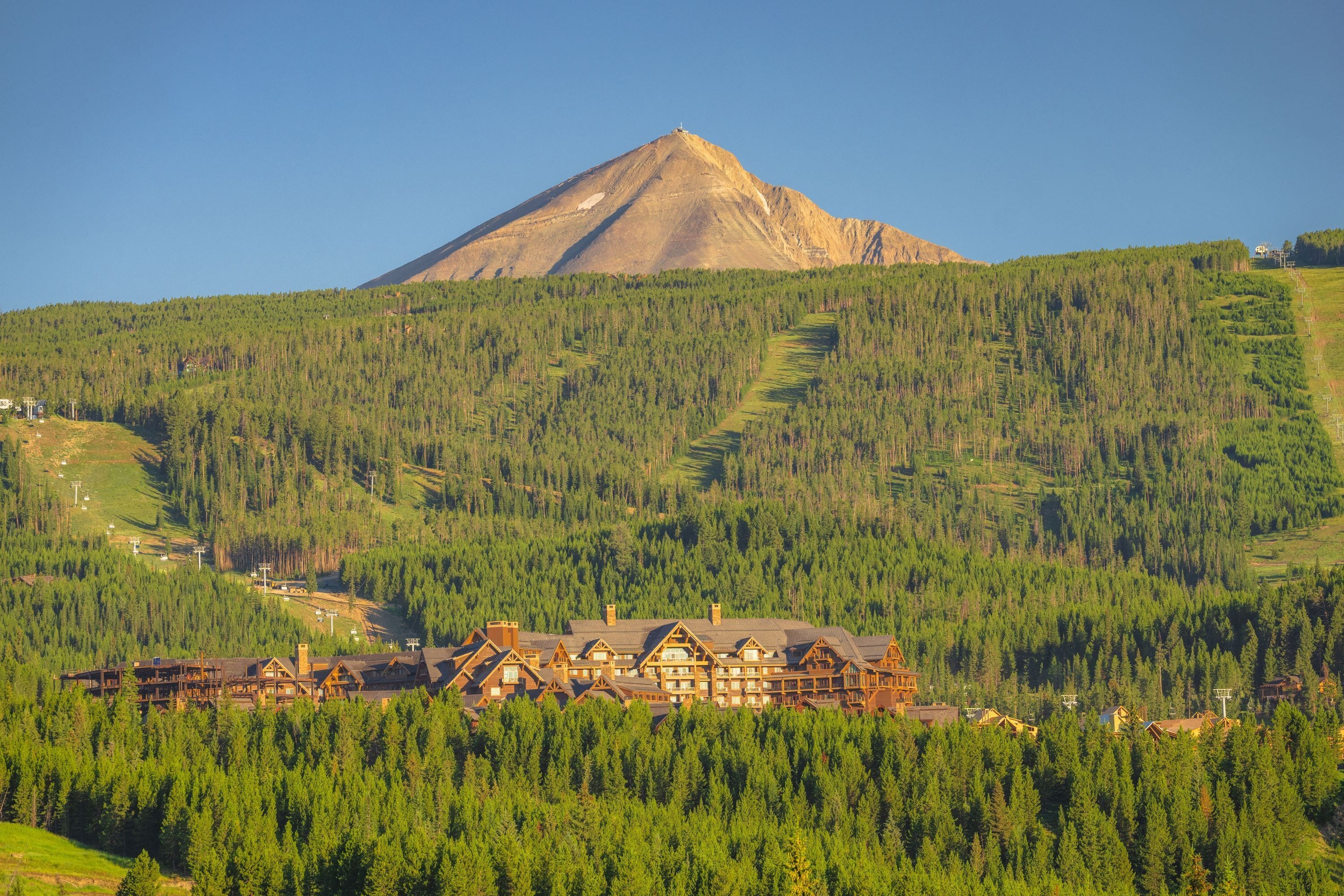 A lodge with a mountain backdrop, surrounded by dense forest.