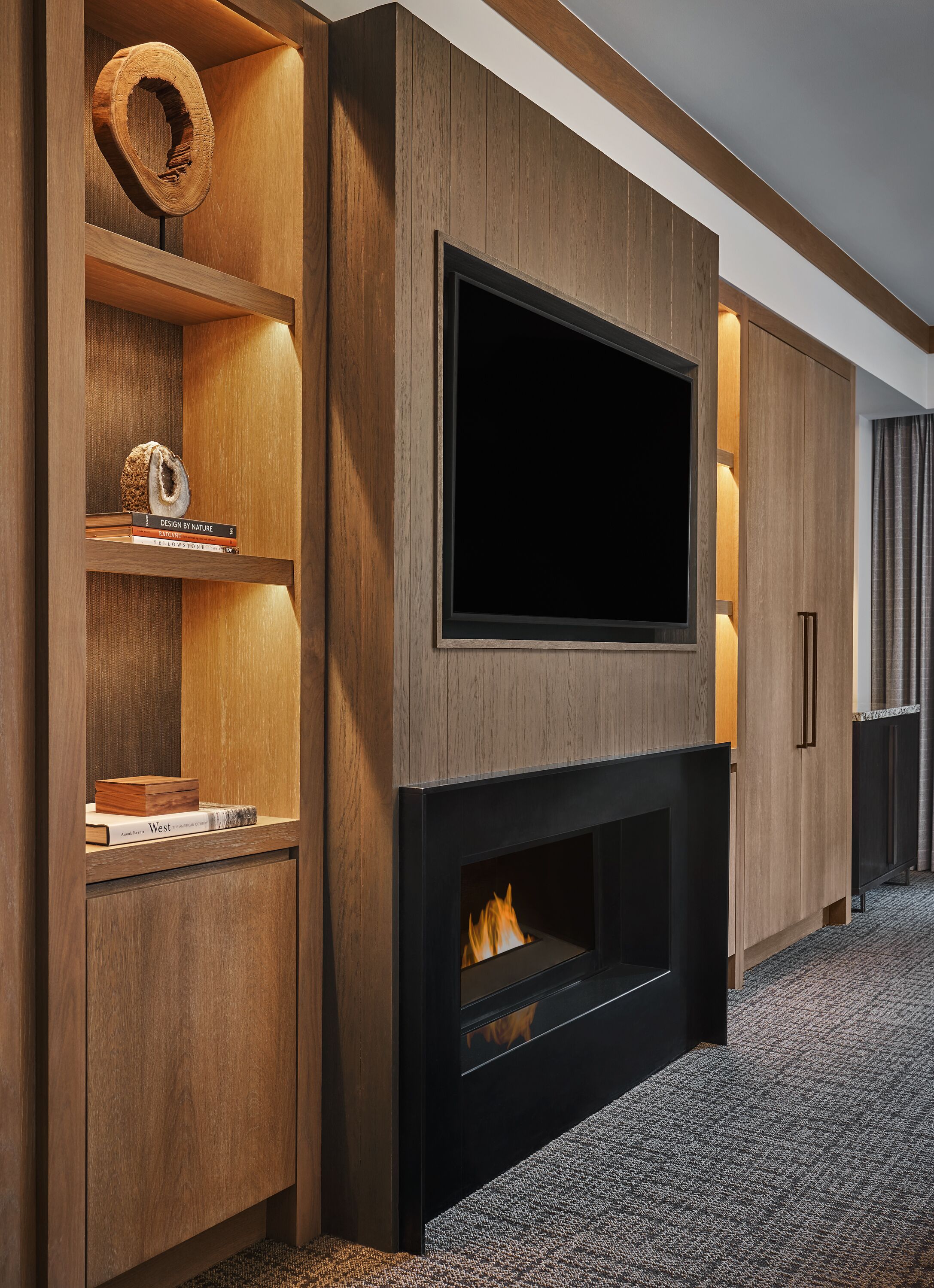 Ein modernes Wohnzimmer mit Flachbildfernseher an einer Holzwand, Kamin und eingebauten Regalen mit Büchern und Dekoration.