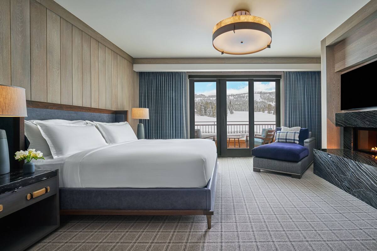 Ein Hotelzimmer mit Bett, Fernseher, Kamin und Blick auf eine verschneite Landschaft.