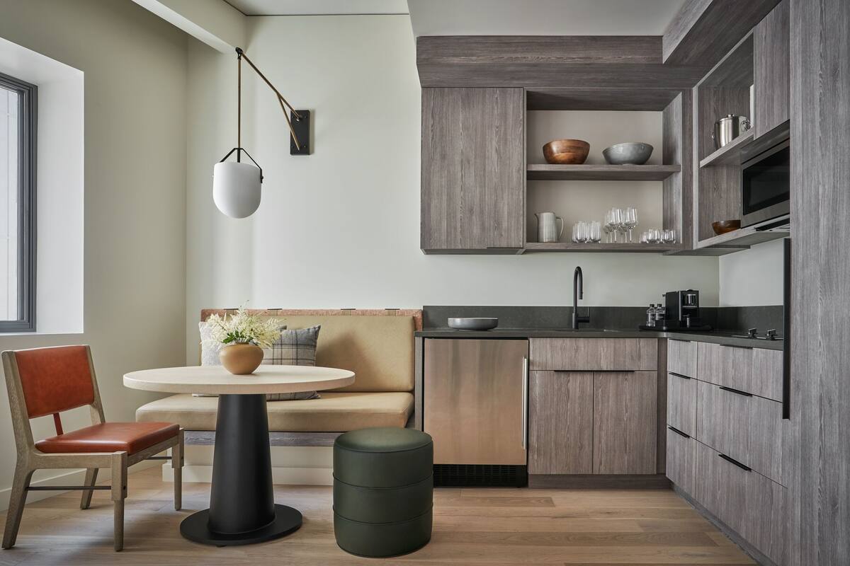 Une cuisine moderne avec des meubles en bois, un coin repas doté d’une table ronde et de chaises, et un four encastré.