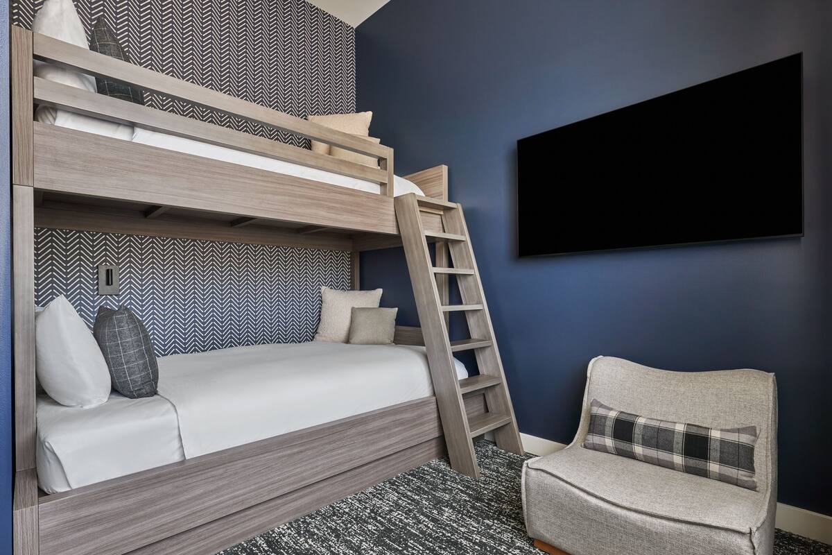 Un lit superposé avec une échelle, un canapé et un téléviseur fixé au mur.