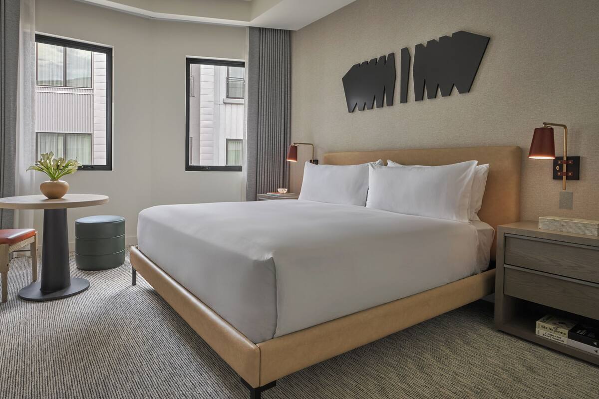 Une chambre d’hôtel avec un grand lit, une chaise, une petite table avec une plante, une table de chevet et une lampe fixée au mur.