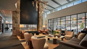 A spacious lobby with a large stone pillar, a fireplace, comfortable seating, and large windows offering city views. - Pendry Park City (Park City)