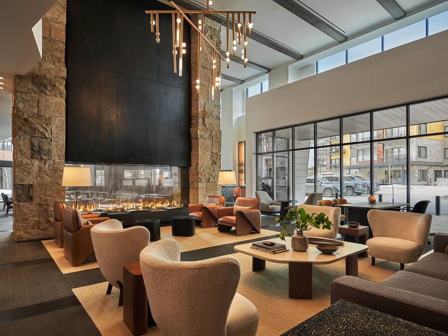 A spacious lobby with a large stone pillar, a fireplace, comfortable seating, and large windows offering city views.