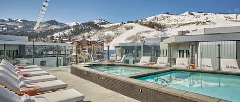 A pool area with lounge chairs, a pool, and a view of snow-covered mountains.