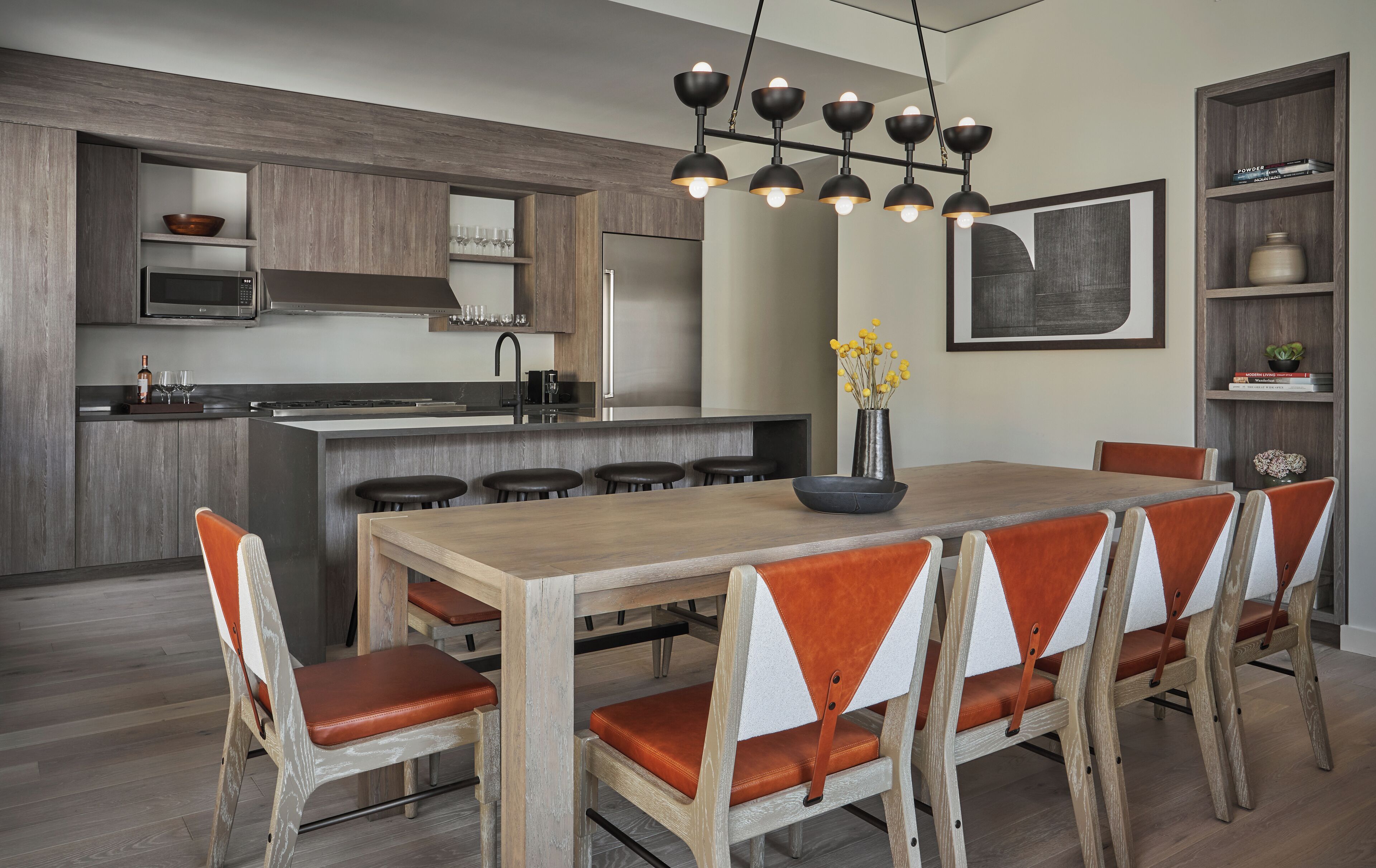 A modern kitchen with a central island, bar stools, a dining table with chairs, and a pendant light fixture.