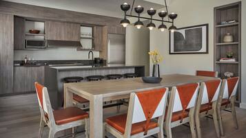 A modern kitchen with a central island, bar stools, a dining table with chairs, and a pendant light fixture.