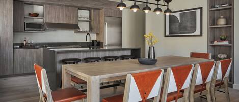 A modern kitchen with a central island, bar stools, a dining table with chairs, and a pendant light fixture.