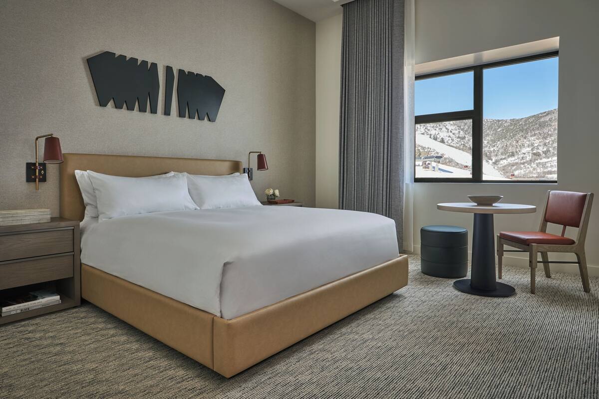 Une chambre d’hôtel avec un grand lit, une petite table, une chaise et une fenêtre donnant sur la montagne.