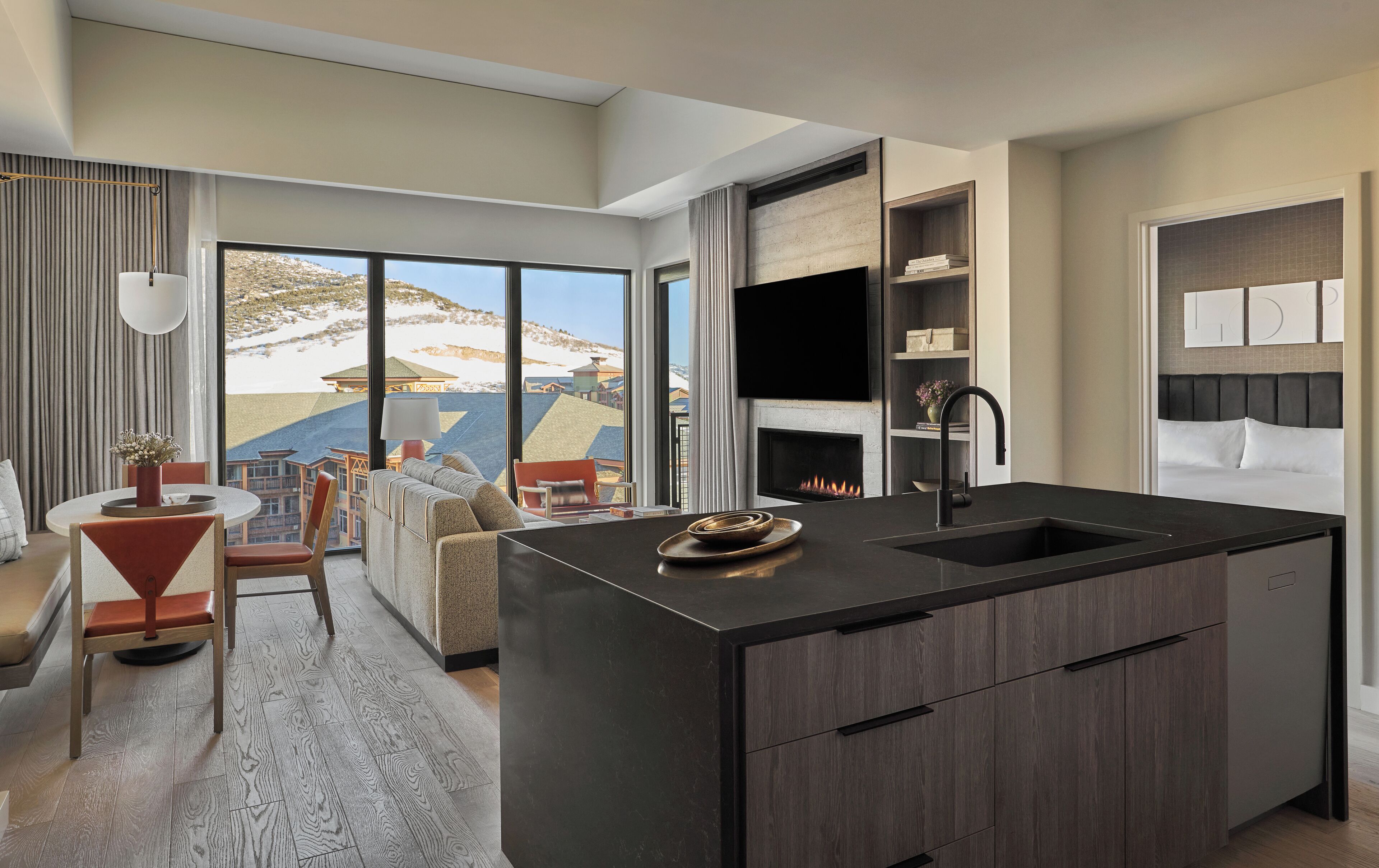 A modern kitchen with a central island, a dining area with a round table and chairs, and a view of a snowy landscape through large windows.