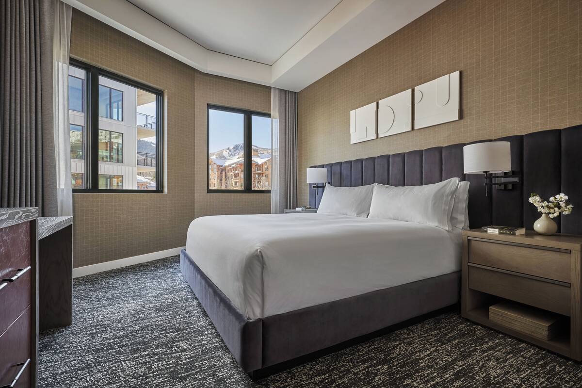 Une chambre d’hôtel avec un grand lit, une table de chevet, un bureau et une fenêtre donnant sur la montagne.