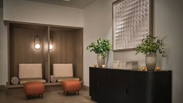 A modern spa room with a wooden bench, two ottomans, a dark wooden cabinet, and a wall-mounted artwork.