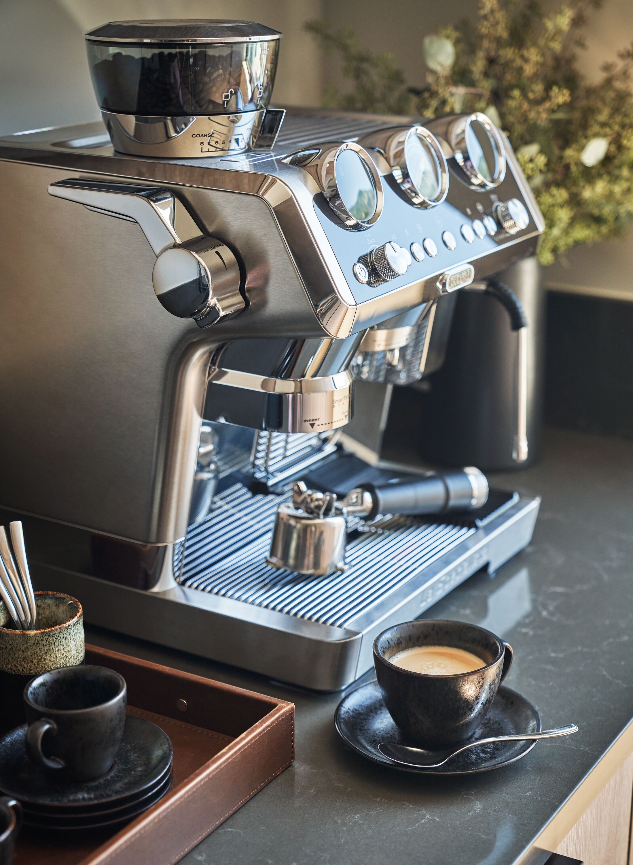 Ammattikäyttöön tarkoitettu espressokone, jossa on digitaalinen näyttö, höyrytin, suodatinkahva ja kuppi kahvia tarjottimella.