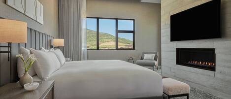 Een moderne hotelkamer met een groot bed, een flatscreen televisie aan de muur, een open haard en uitzicht op de omgeving.