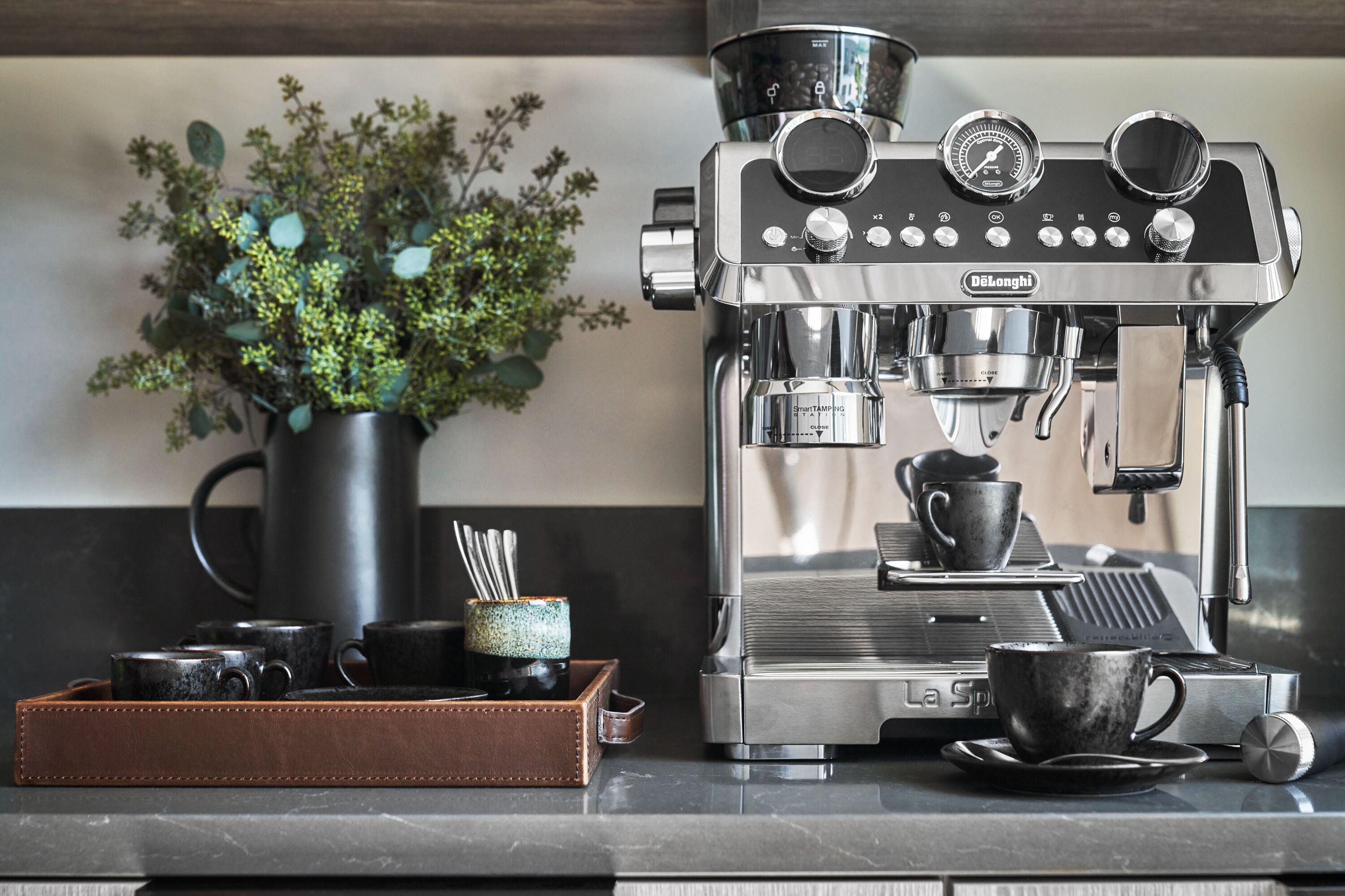 A modern coffee machine with a digital interface, a cup of coffee on the counter, and a small plant in the background.