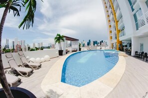 A rooftop pool with lounge chairs, a palm tree, and a city skyline in the background. - Modern Apartment in a Luxurious Residential Unit in the heart of the city (Panamá)