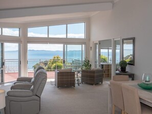 A spacious living room with large windows, a balcony, and a view of the sea. - Executive Accommodation with World Class Views (Coopers Beach)