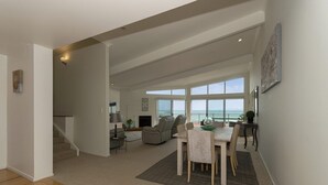 Ampla sala de estar com mesa de jantar, sofás e vista para o mar.