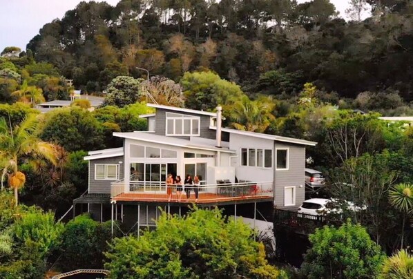 A modern two-story house with a balcony, surrounded by lush greenery and hills. - Executive Accommodation with World Class Views (Coopers Beach)