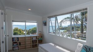 Quarto com uma grande janela que oferece vista para o mar e montanhas, uma estante embutida e um espaço de estar acolchoado.