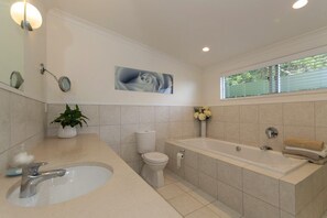 A modern bathroom with a bathtub, toilet, sink, and a window with blinds. - Executive Accommodation with World Class Views (Coopers Beach)