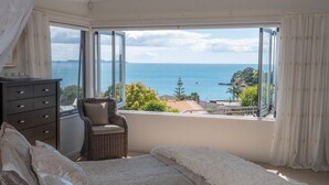 Quarto com uma grande janela que oferece vista para o mar e vegetação.