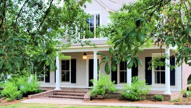 A two-story house with a covered porch, brick steps, and a well-maintained lawn.
