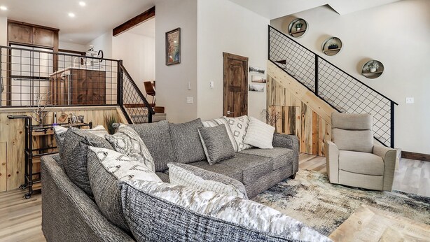 En stue med en grå hjørnesofa, en beige lænestol og en trappe med gelænder af metal.