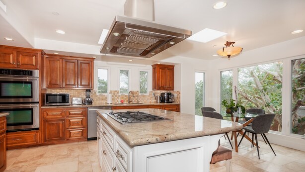 A modern kitchen with wooden cabinets, a central island, and a large window offering a view of trees.